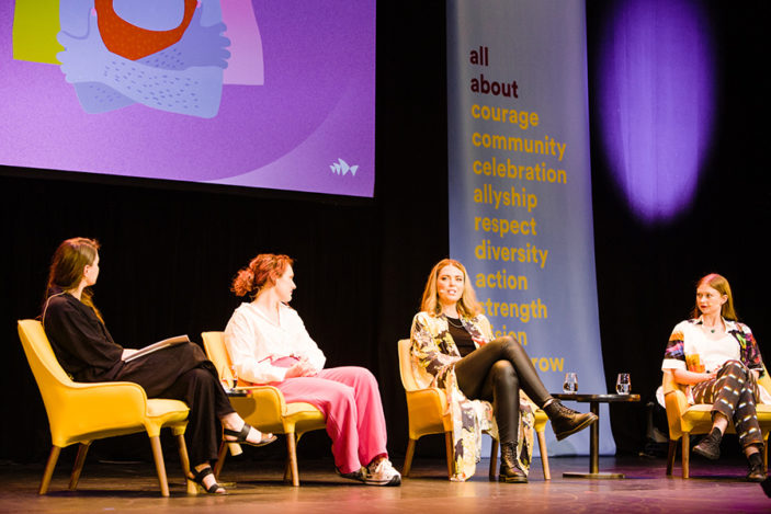 Four women are seated on stage in conversation.