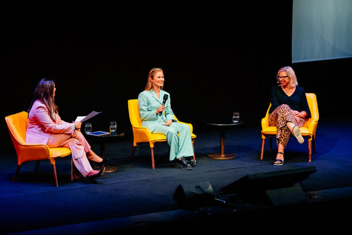 Three women are seated on stage having a conversation.