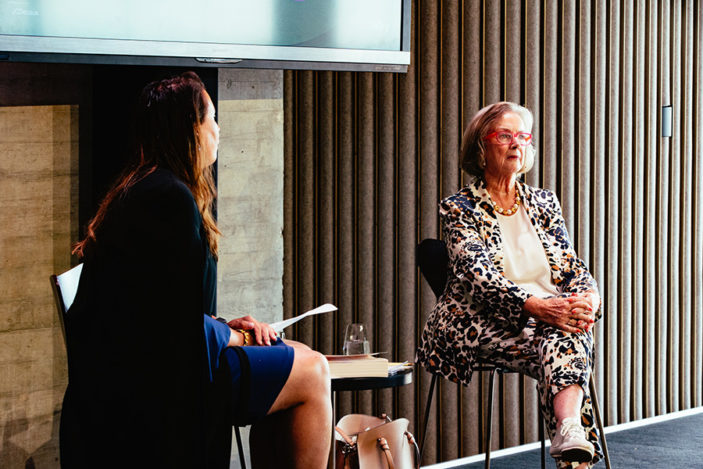 Two women sit on stage in conversation.