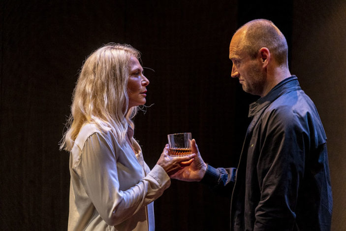 A woman and a man face each other as he hands her a drink.