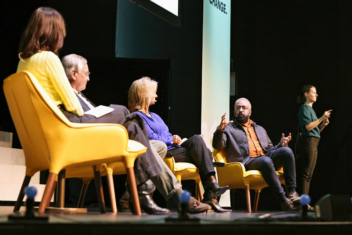 Two women and two men are seated on a stage having a conversation.