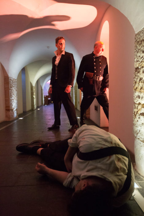 Two men stand over the body of an unconscious man.