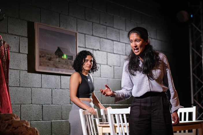 Two women have a heated exchange around a kitchen table.