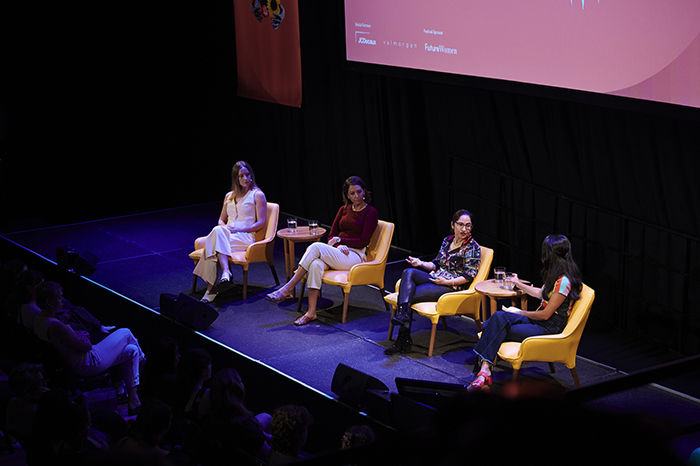 Four women sit on stage in front of a crowd having a conversation.