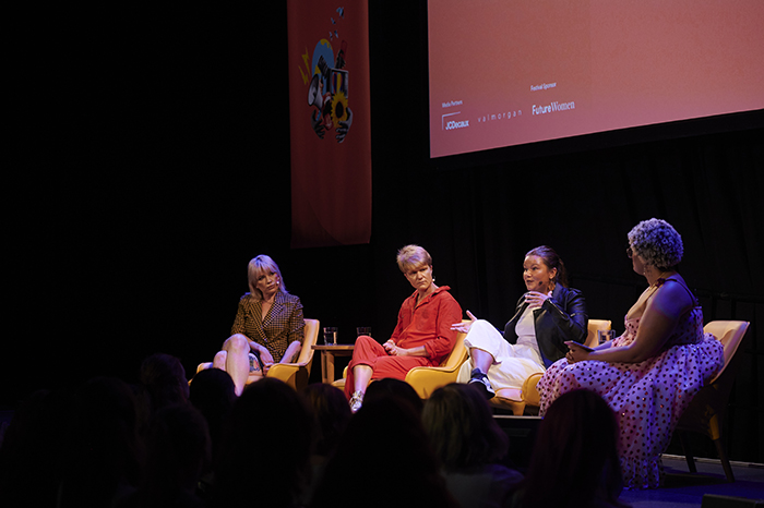 Four women sit on a stage in front of an audience having a conversation.