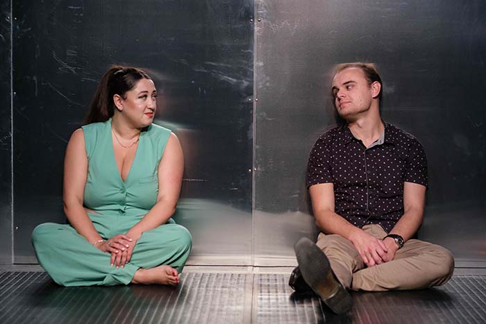 A woman and a man sit leaning against the back of a lift, smiling at each other.